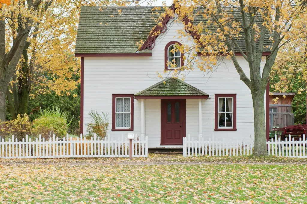 A white house with a picket fence under maple trees
